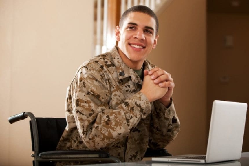 Smiling soldier in wheelchair using laptop.