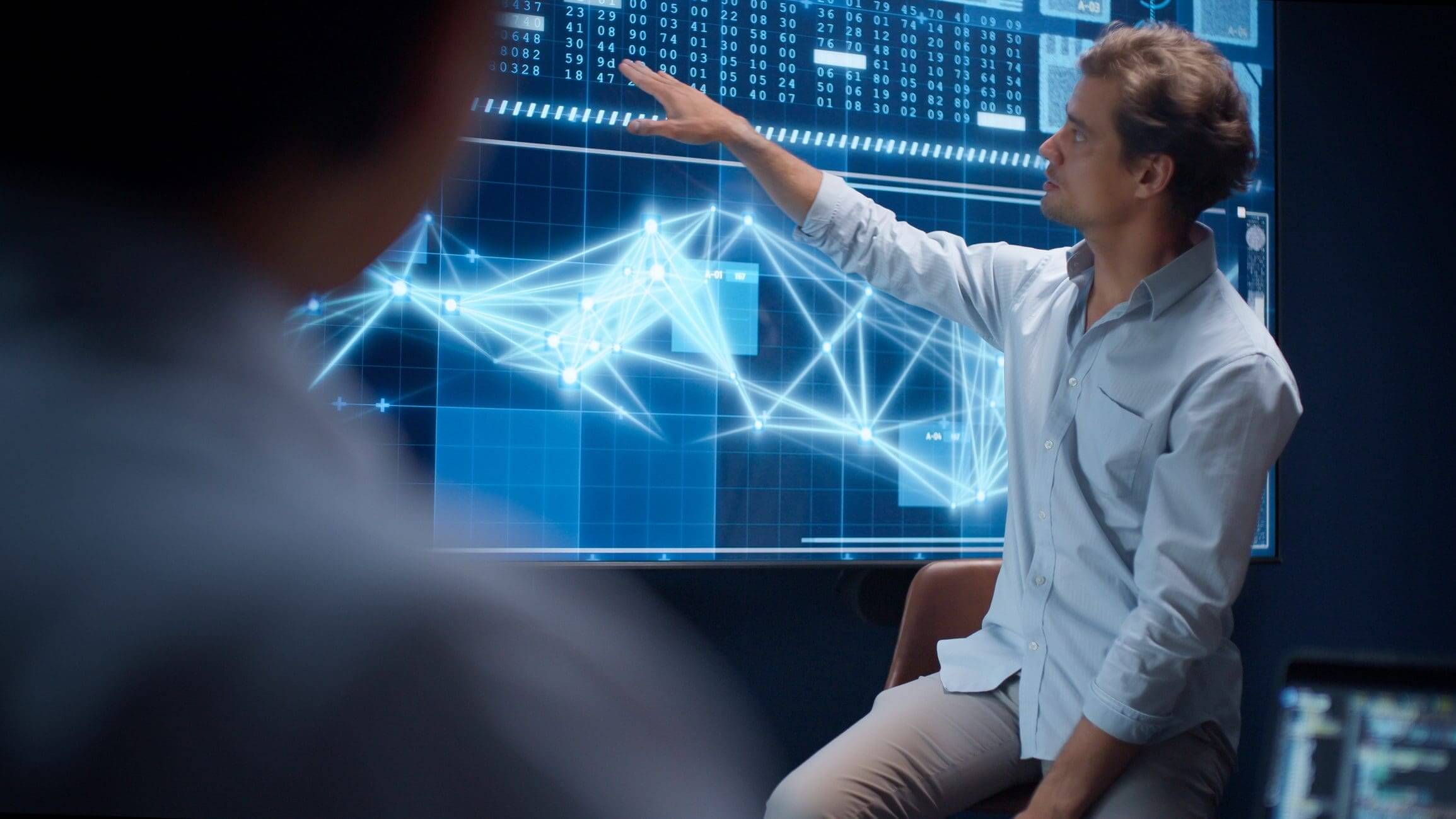 Man presenting data with digital network graphics on a large screen.