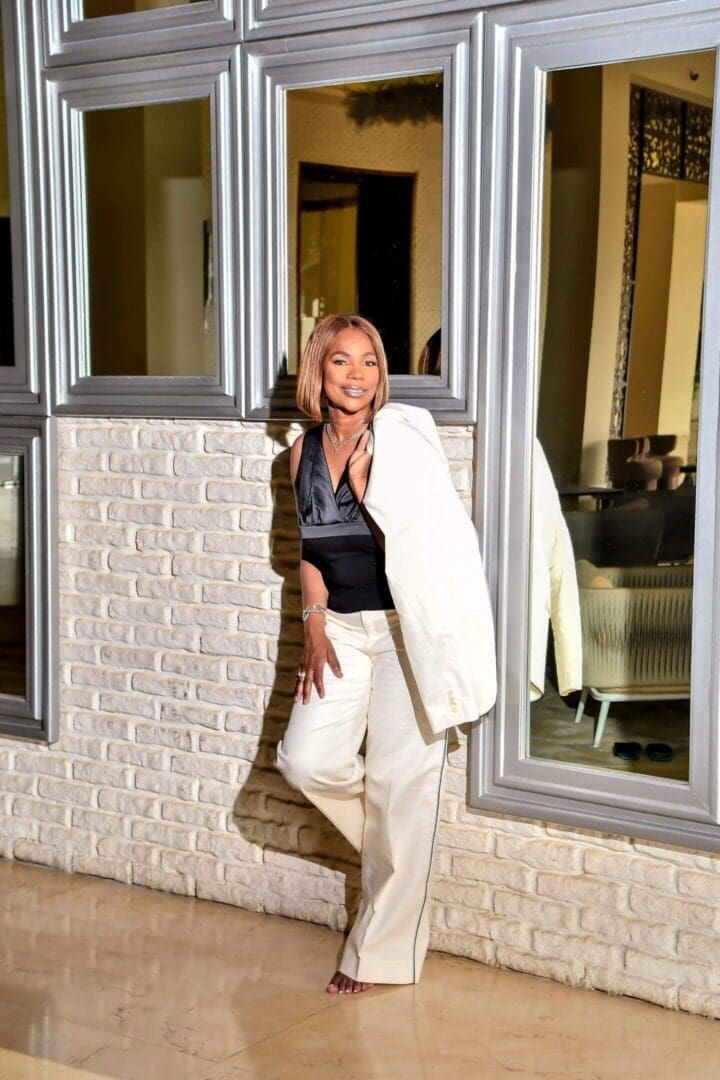 Confident woman in stylish white suit posing by a windowed wall.