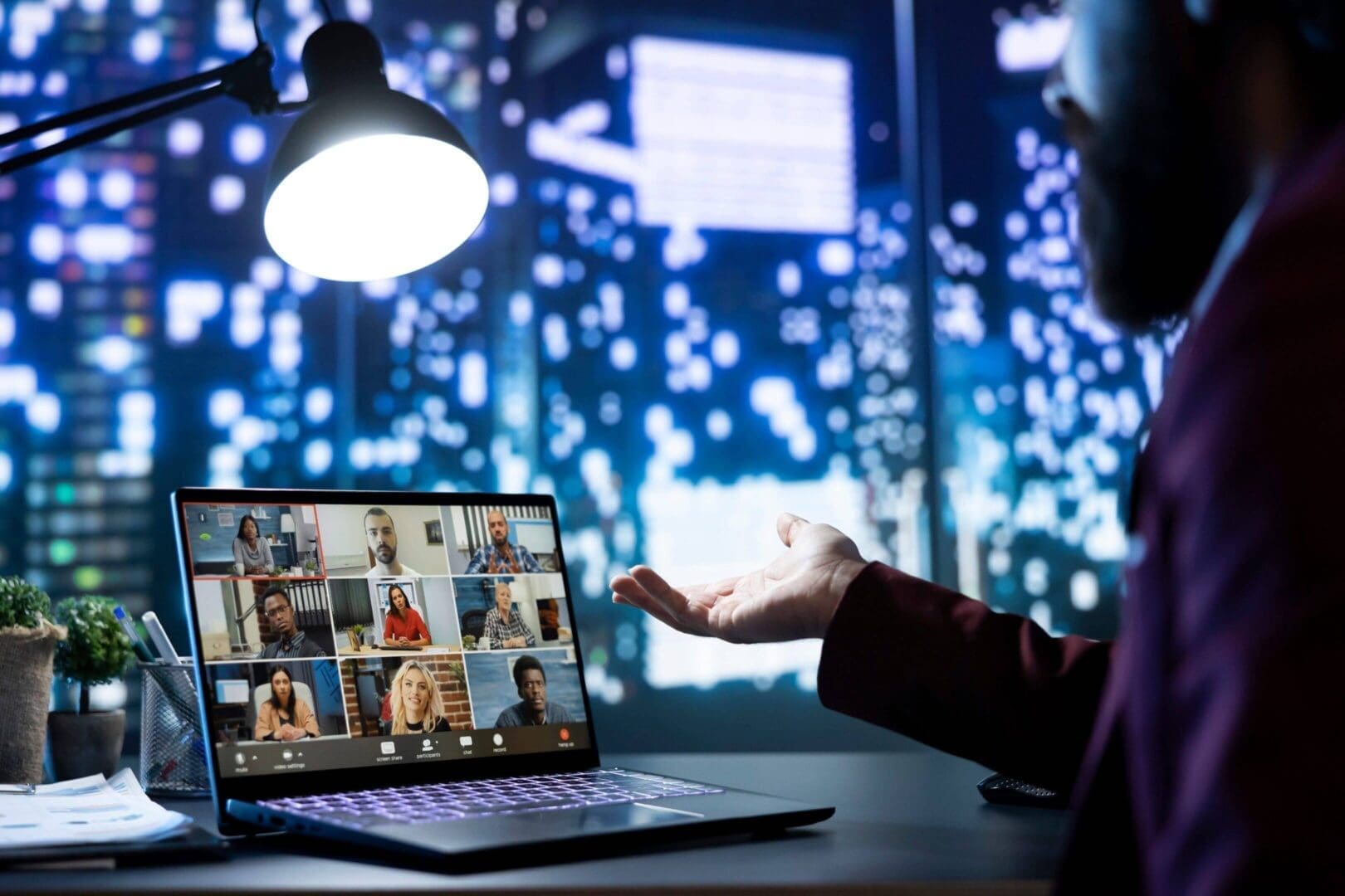Person gesturing towards laptop with virtual meeting on screen.