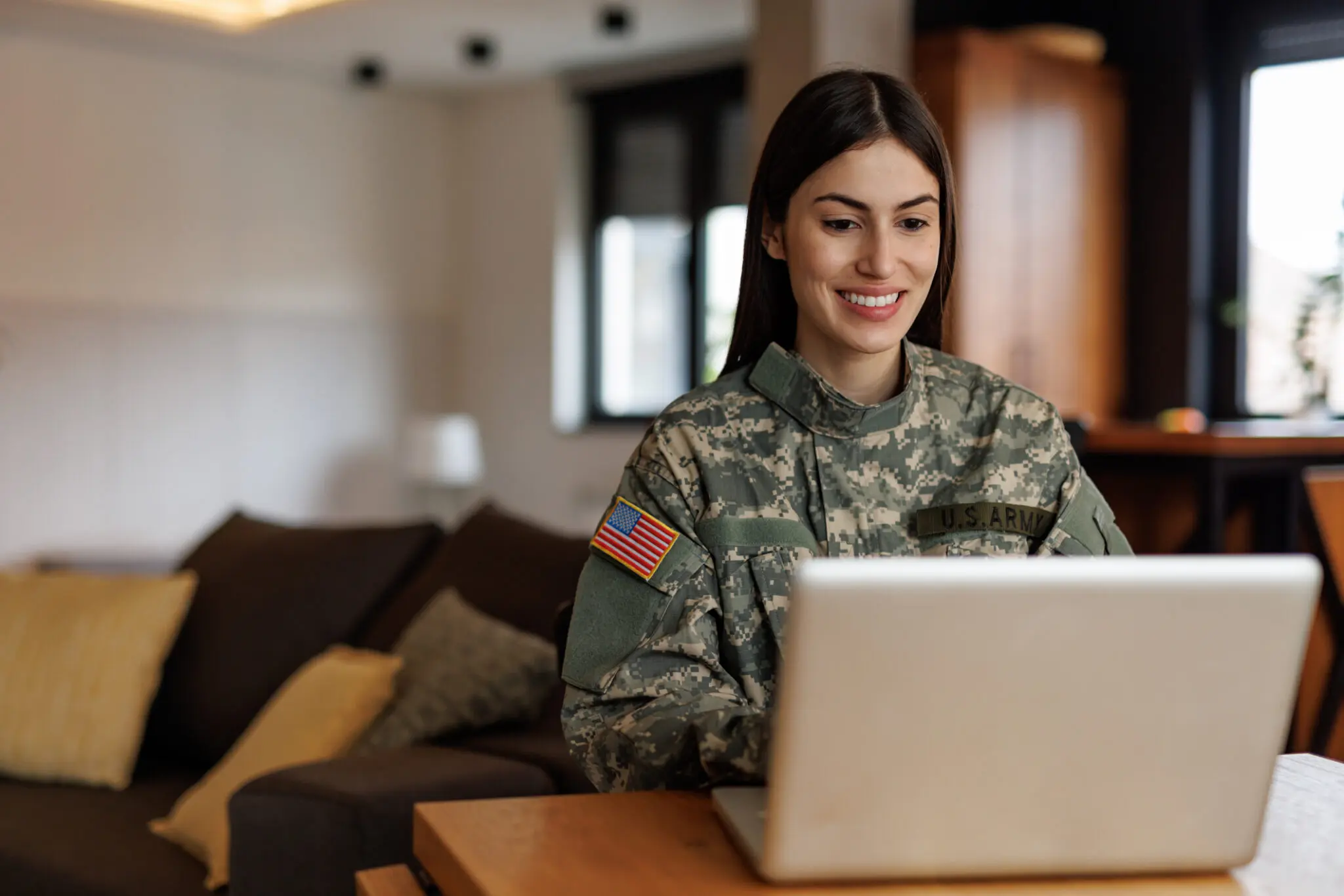 A female soldier in uniform using a laptop indoors.