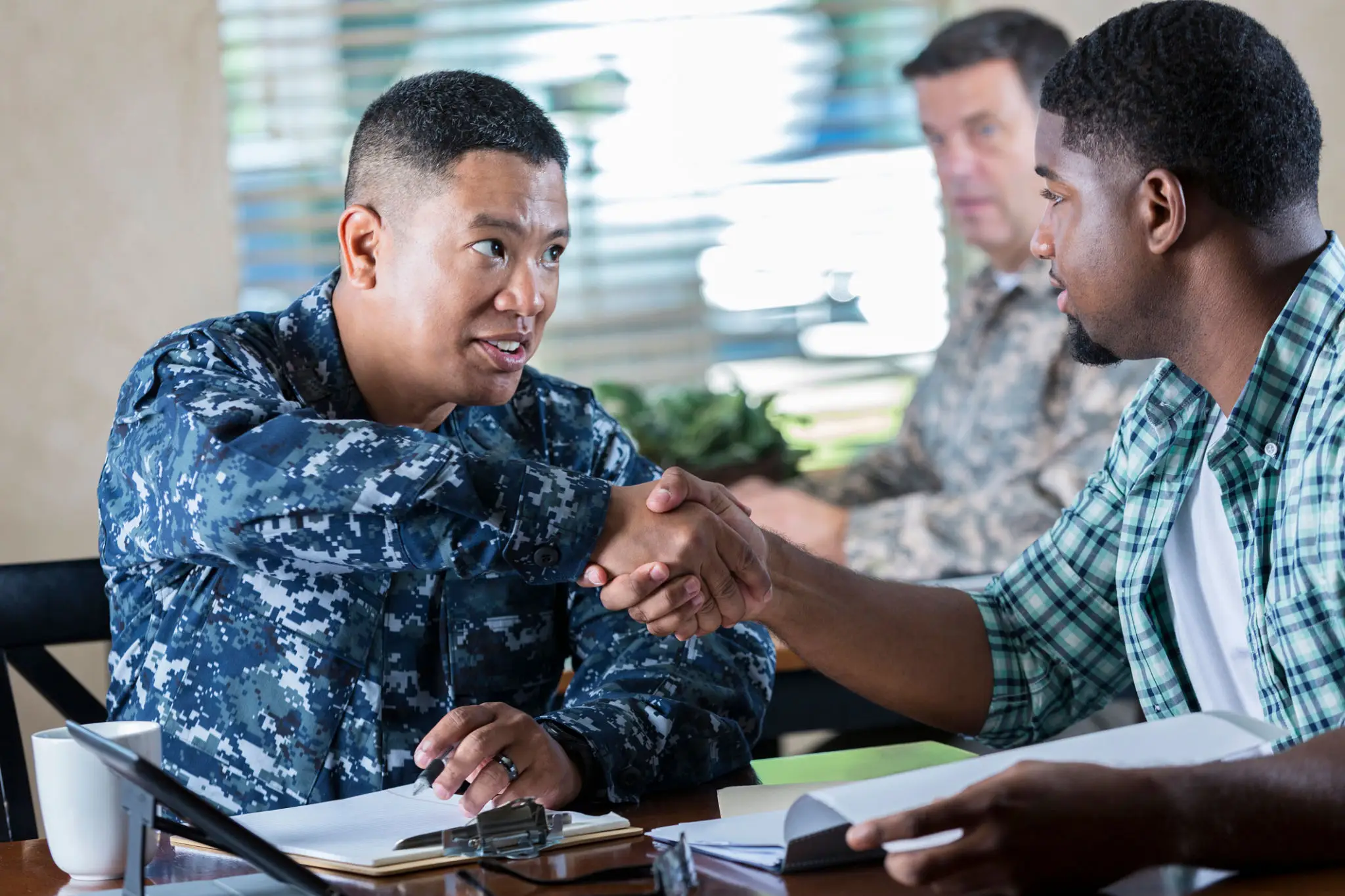 Military personnel and a civilian shake hands during a meeting.